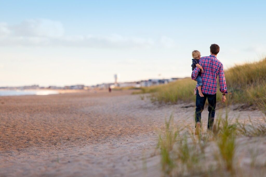 a man carrying his baby while walking on the beach